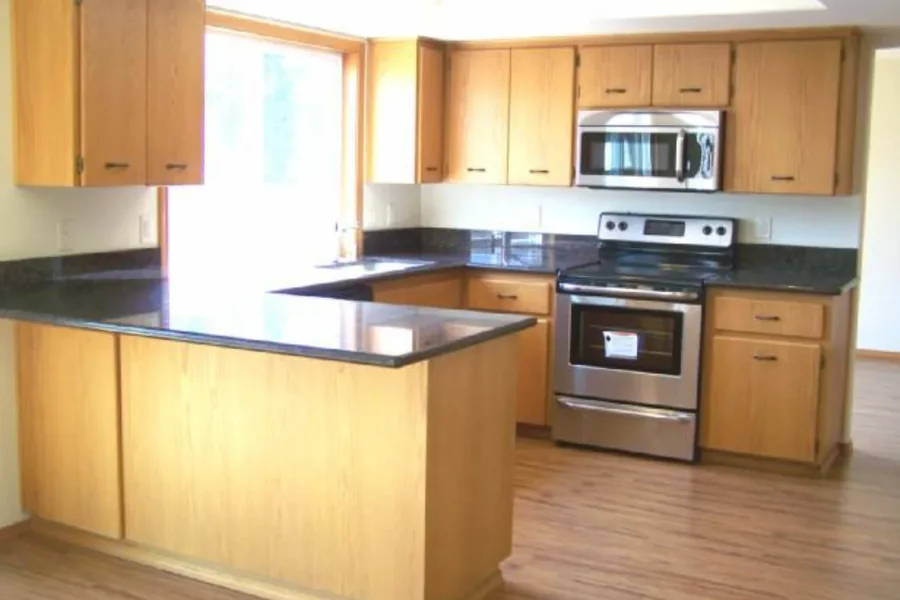 Original photo of a dated kitchen with honey maple cabinets and black granite counters