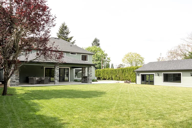 Back of a remodeled home with a covered stone patio and lawn, by JDI Construction